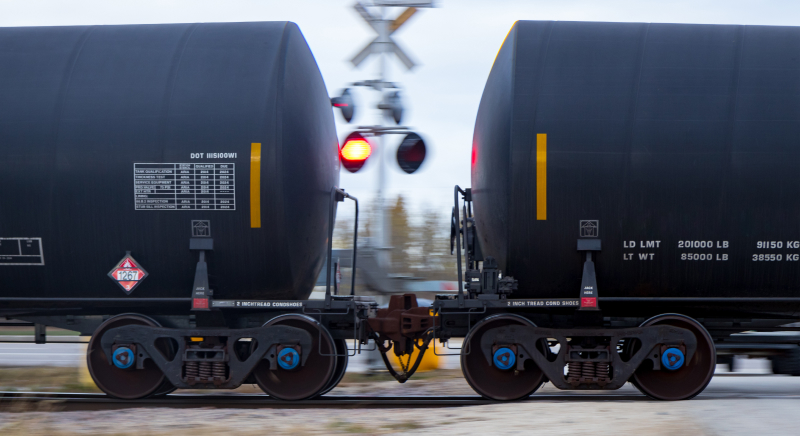 Black freight train transporting oil, moving at high speed on railway tracks.